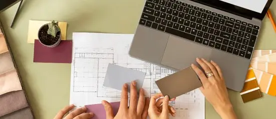 Hands sketching a layout beside a laptop and colour swatches